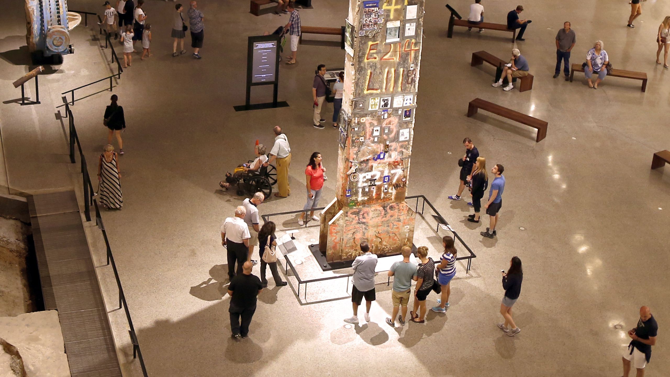 The Last Column towers over Museum visitors gathered around it. The thirty-six-foot-tall steel beam is covered in pictures and tributes left by recovery workers at Ground Zero. Off to the left, visitors observe a river water valve that was recovered from under the World Trade Center.