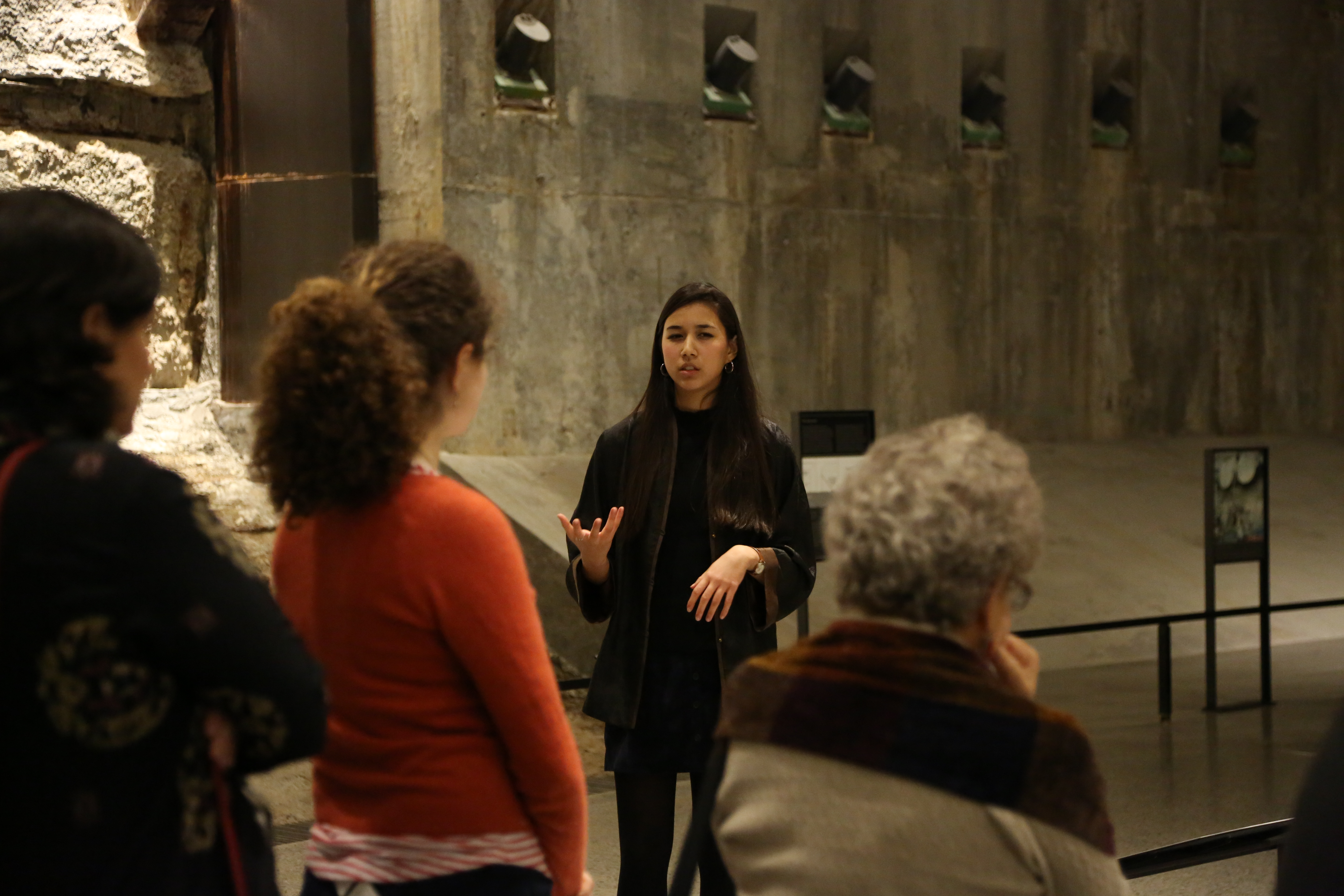 9/11 Memorial Museum ambassador Annalee Tai leads a Museum tour beside the slurry wall. Three visitors are in the foreground listening to her.