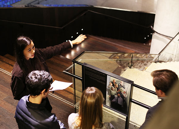 Student ambassador Annalee Tai leads a tour through the 9/11 Memorial Museum. She points to the Survivors’ Staircase as several people watch on.