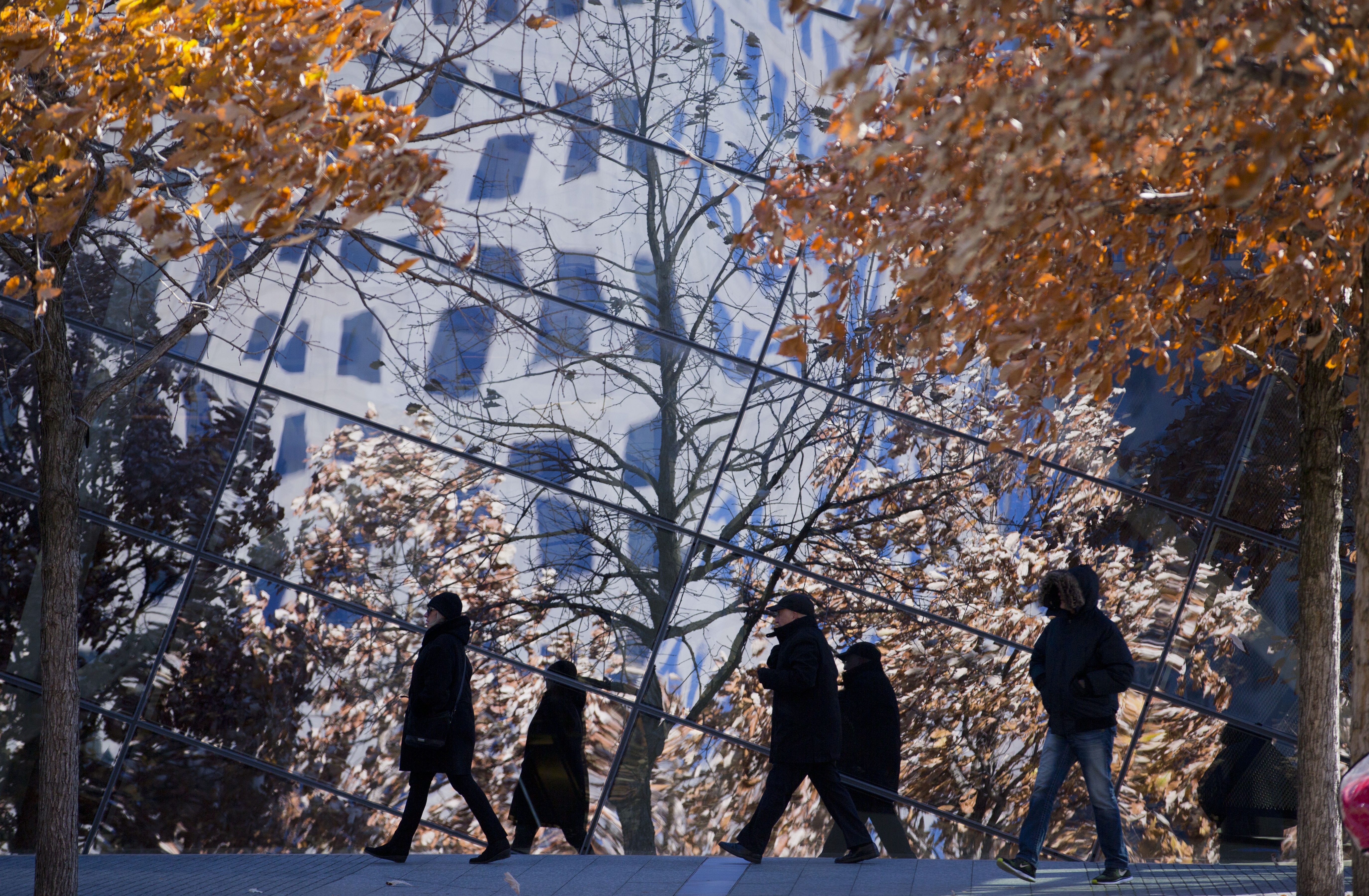 Visitors wearing winter jackets pass by the glass facade of the 9/11 Memorial Museum.