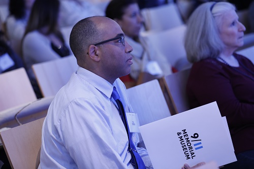 An educator looks towards the stage in the Museum auditorium. He is holding a 9/11 Memorial & Museum folder and  wearing a tie and dress shirt.