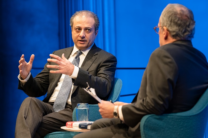 A man gestures with his hands in conversation with another man on a blue stage.