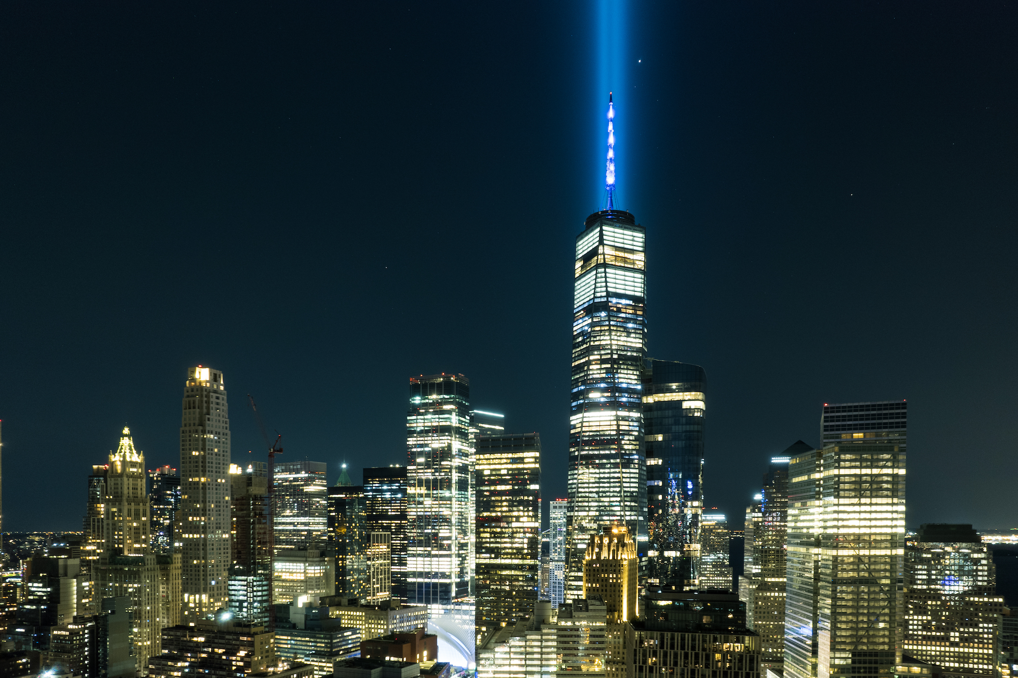 Two beams of blue light emanate from One World Trade Center, against a dark sky
