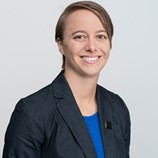 Woman with short light brown hair in navy blue blazer and brighter blue shirt