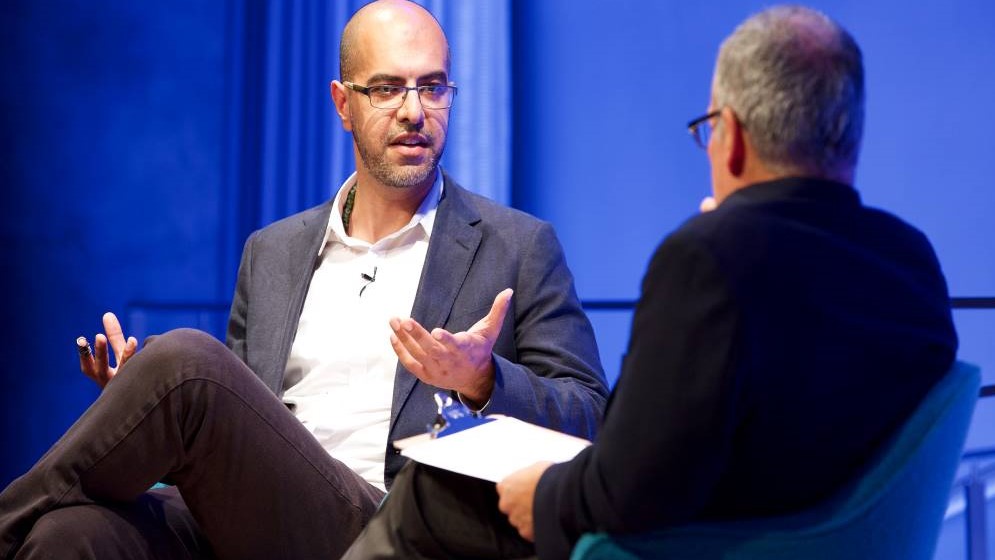 Author and news commentator Haroon Moghul gestures as he speaks onstage at the Museum Auditorium. In the foreground is Clifford Chanin, the executive vice president and deputy director for museum programs. 