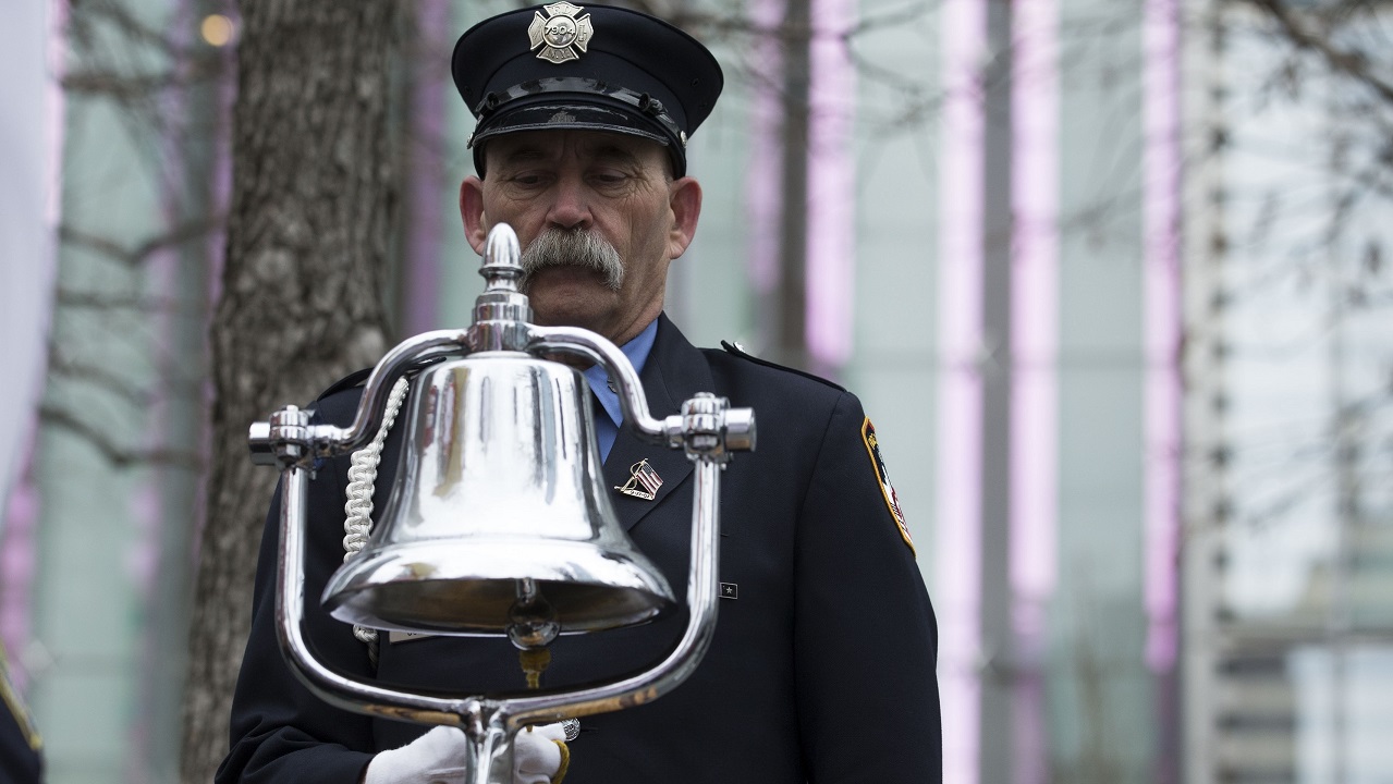 A mustachioed firefighter in a formal FDNY outfit rings a silver bell.