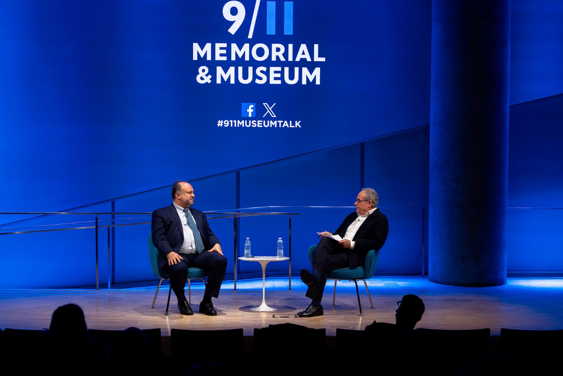 Bernard Haykel and Cliff Channing speak together on stage. A wide lens shows the stage and 9/11 Memorial & Museum logo