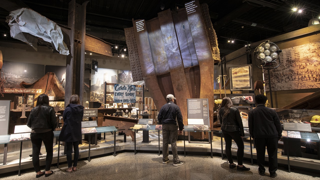 Visitors look at artifacts in the Museum's Historical Exhibition, including a large steel trident from a facade of the Twin Towers.