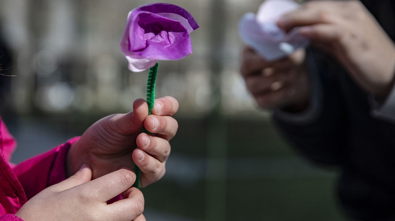 A child's hands hold a purple paper flower.