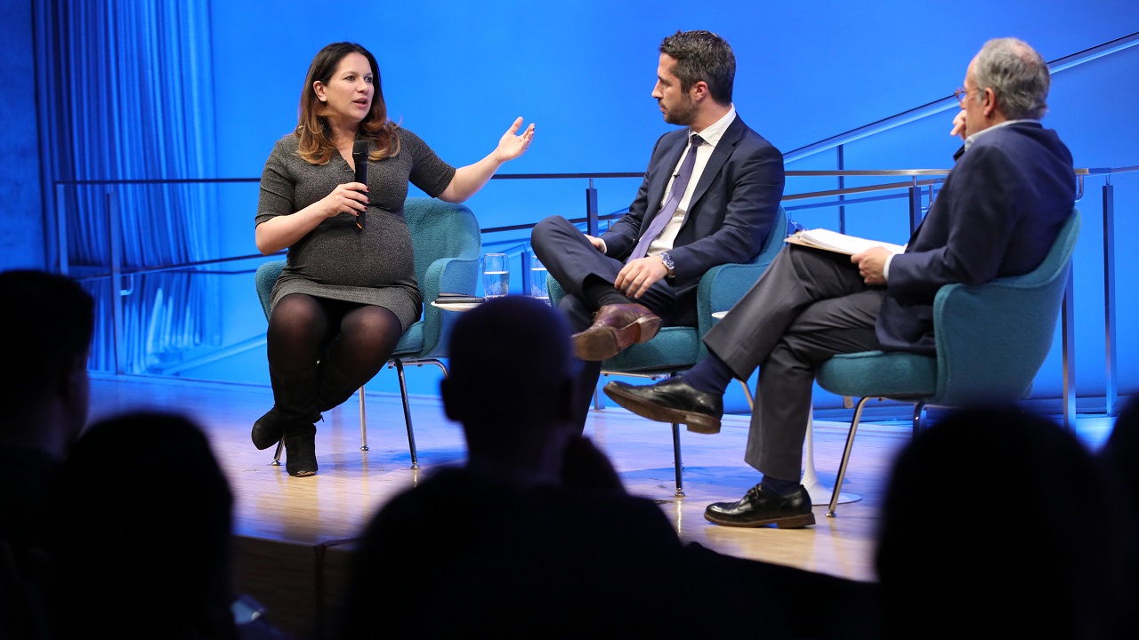 New York Times foreign correspondent Rukmini Callimachi and Lorenzo Vidino, director of the George Washington University Program on Extremism, are onstage at the Museum Auditorium, along with Clifford Chanin, the executive vice president and deputy director for museum programs. Callimachi is speaking as the two men look on. She is holding a microphone in her right hand as she gestures with her left hand. Vidino and Chanin listen on with their legs crossed.