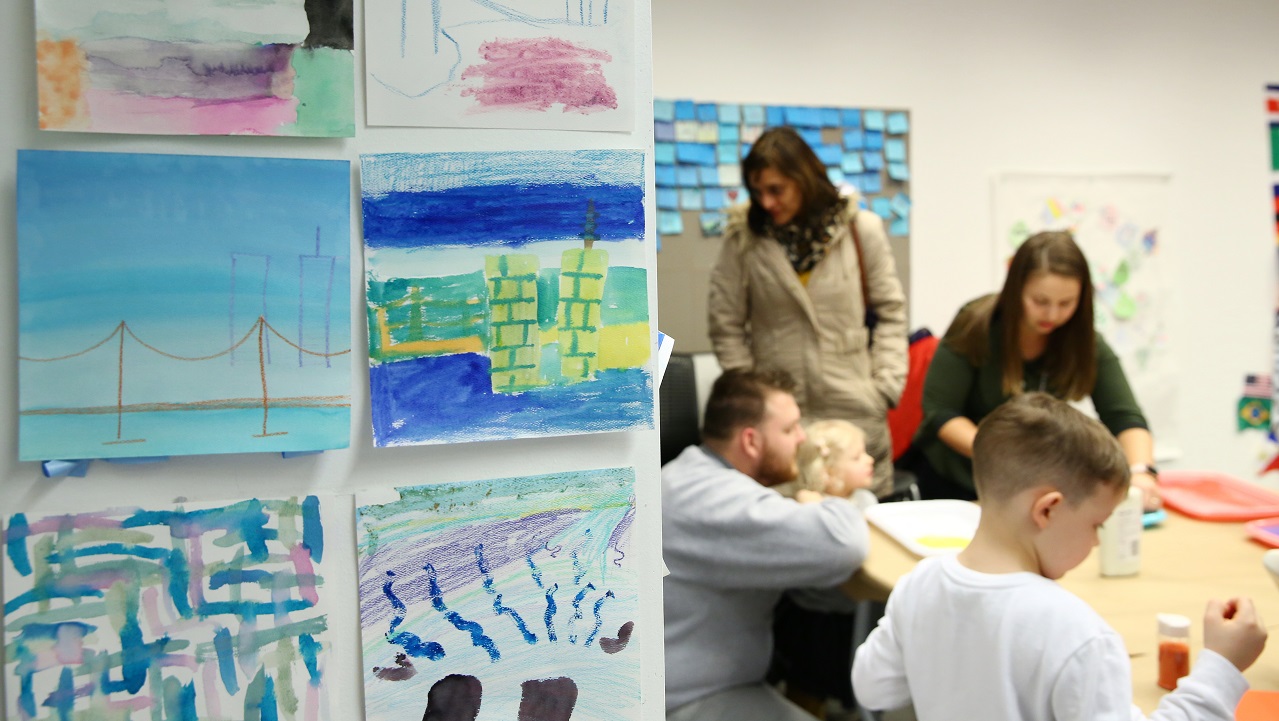 This photograph frames children's artwork and children working on an art activity in the Museum's classroom space.