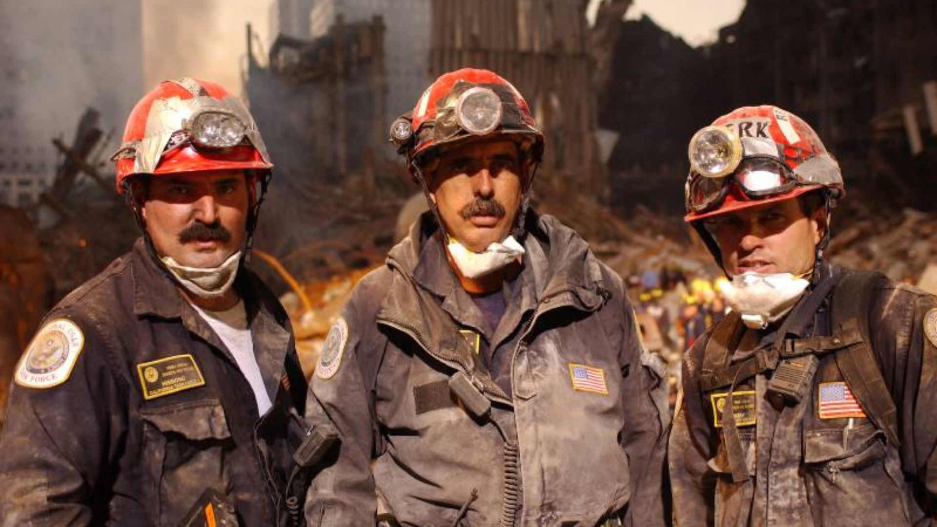 Three men in red hard hats, covered in dust, stand on the pile at Ground Zero