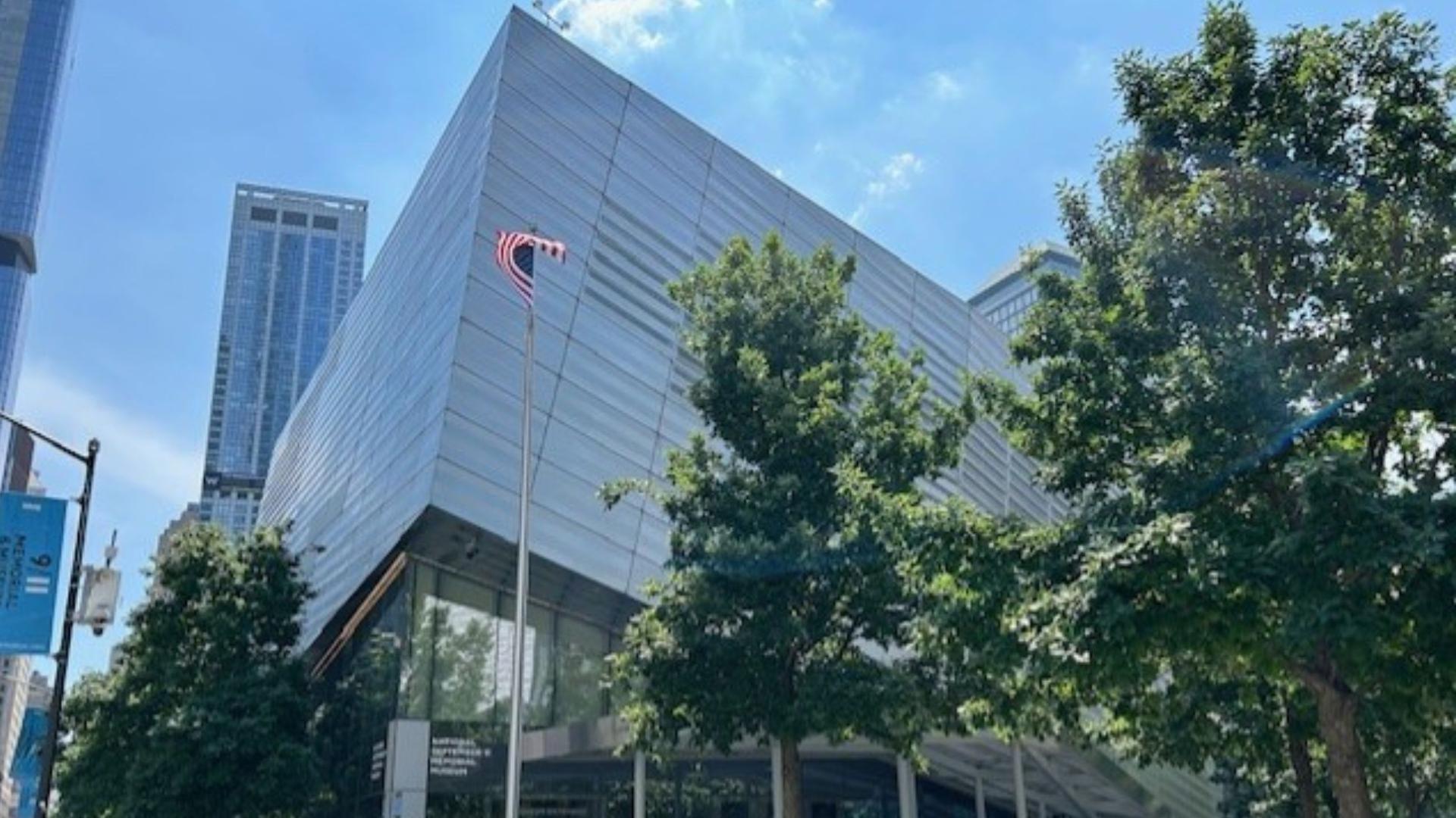 Exterior of the Museum against a blue sky, with green trees in the foreground and an American flag swaying in the breeze