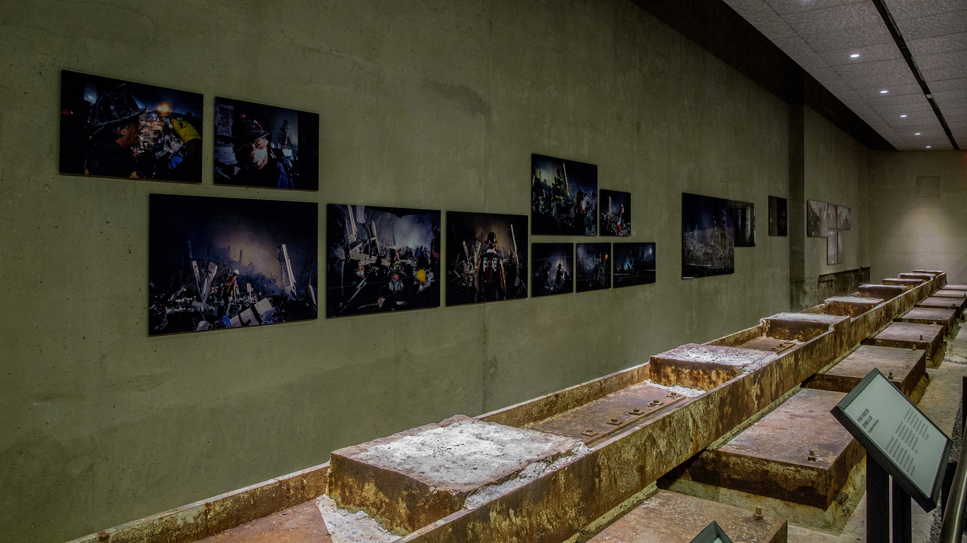 Several large photographs mounted on a gallery wall behind rusted steel beams.