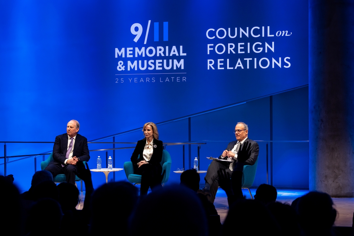 Three people sit on stage in front of a blue background 