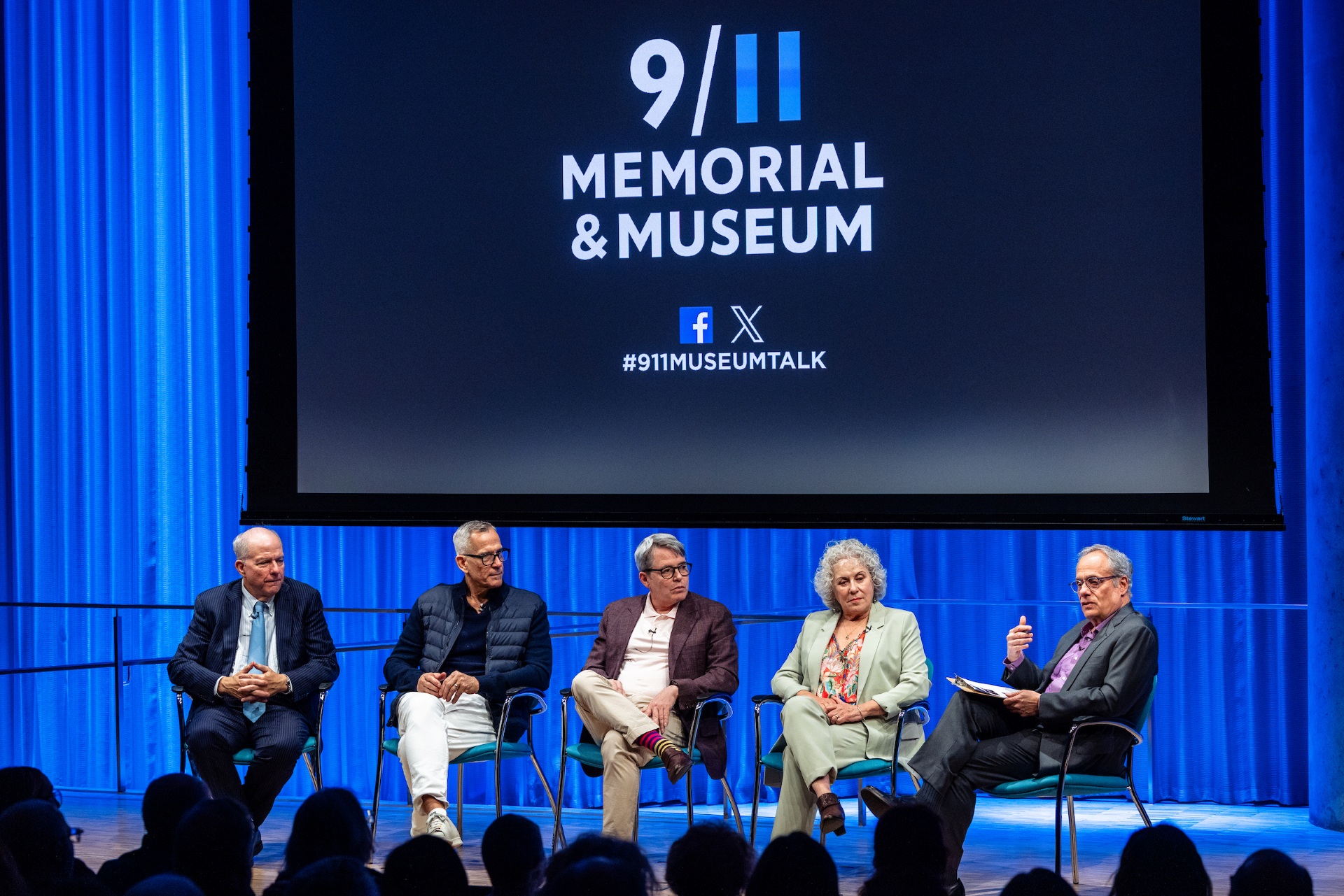 A group of five people sit on stage under the 9/11 Memorial & Museum logo