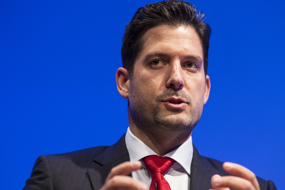 In this close-cropped photograph, a man in a red tie gestures with his hands.