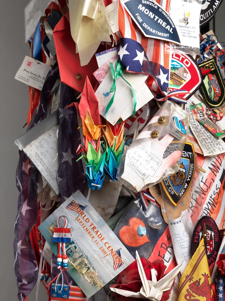 Close up shot of Lady Liberty sculpture covered with first responder badges, inspirational messages, mini paper cranes, and patriotic memorabilia.