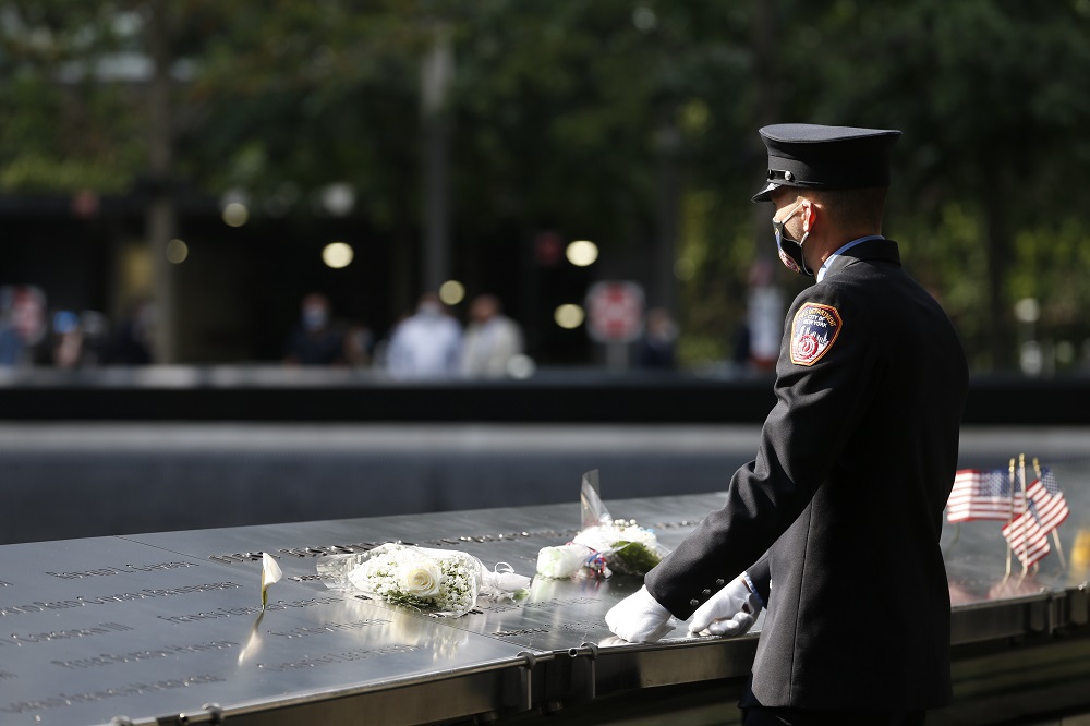 A first responder in dress uniform stands over flower tributes placed on the memorial parapets.