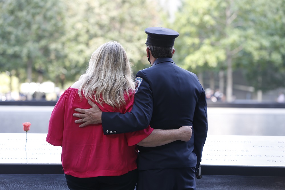 A man in dress uniform and a woman embrace on the Memorial plaza.