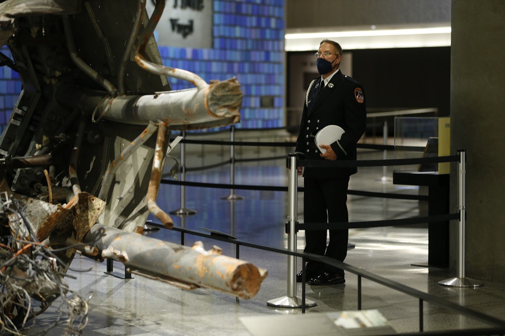 A first responder in dress uniform stands looking a a remnant of the North Tower's antenna in the Museum.