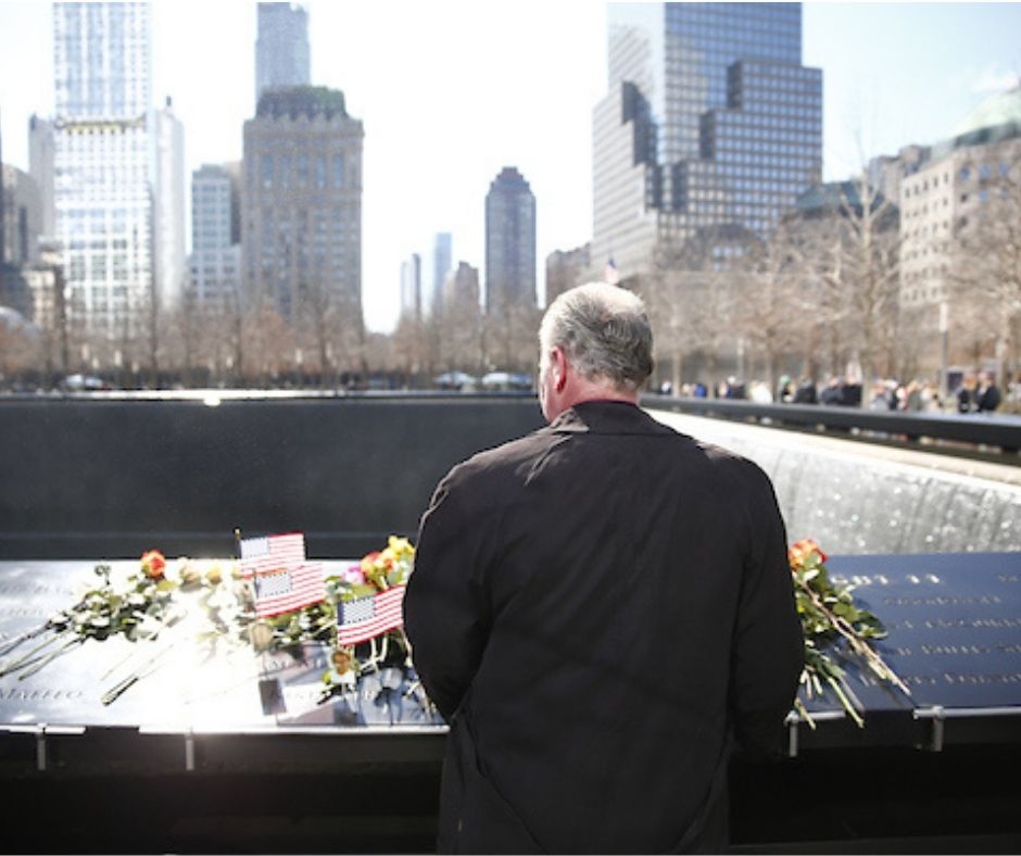 Back view of a man in a dark coat looking at flowers on the Memorial