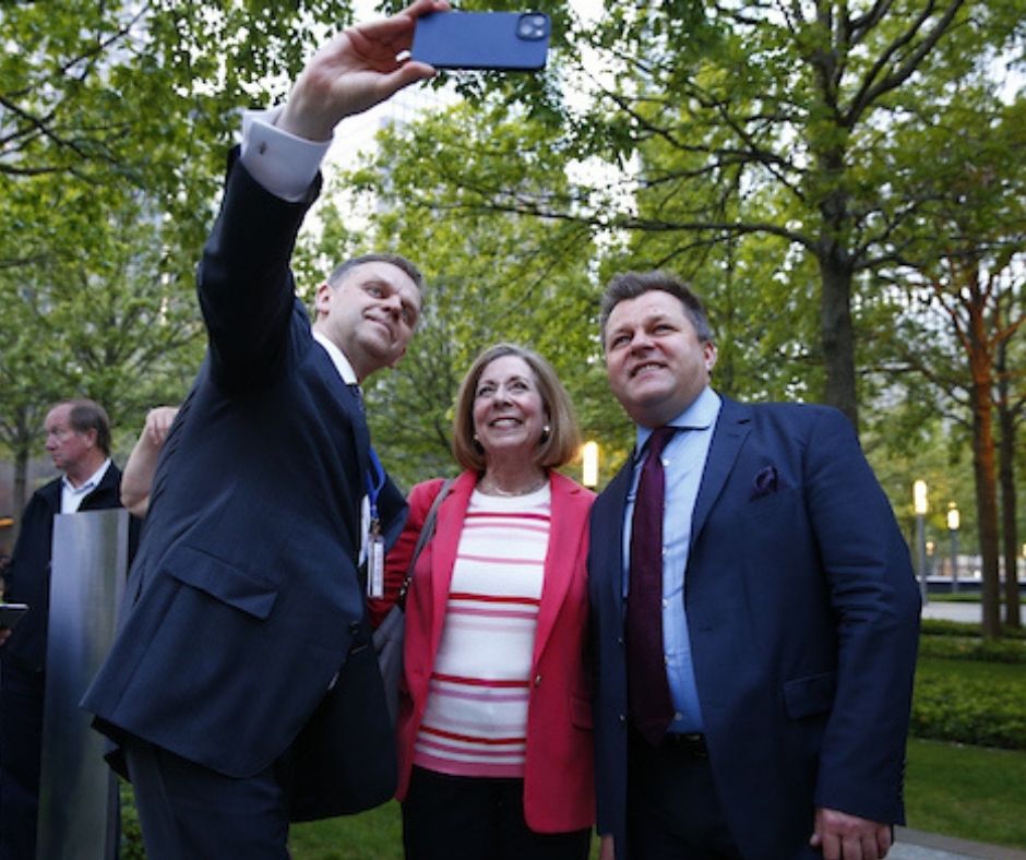 Two men in dark suits pose for a selfie with a woman in a red jacket