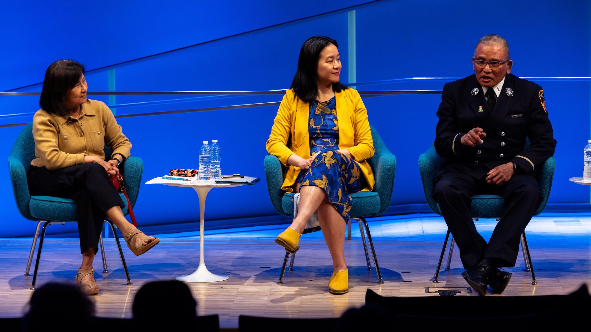 Three seated panelists on stage against a bright blue backdrop. 