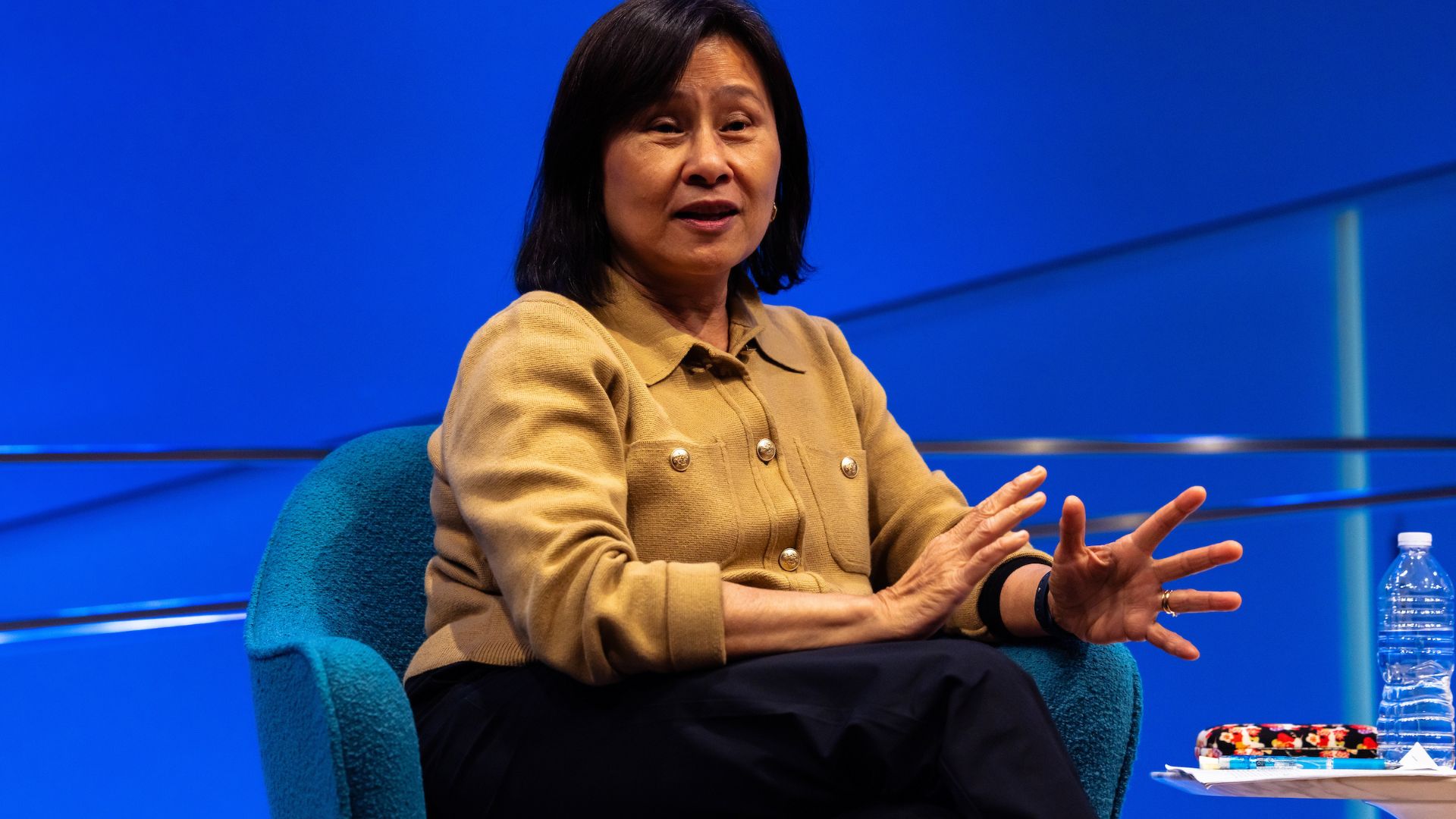 A seated panelist speaks on stage against a bright blue backdrop. 
