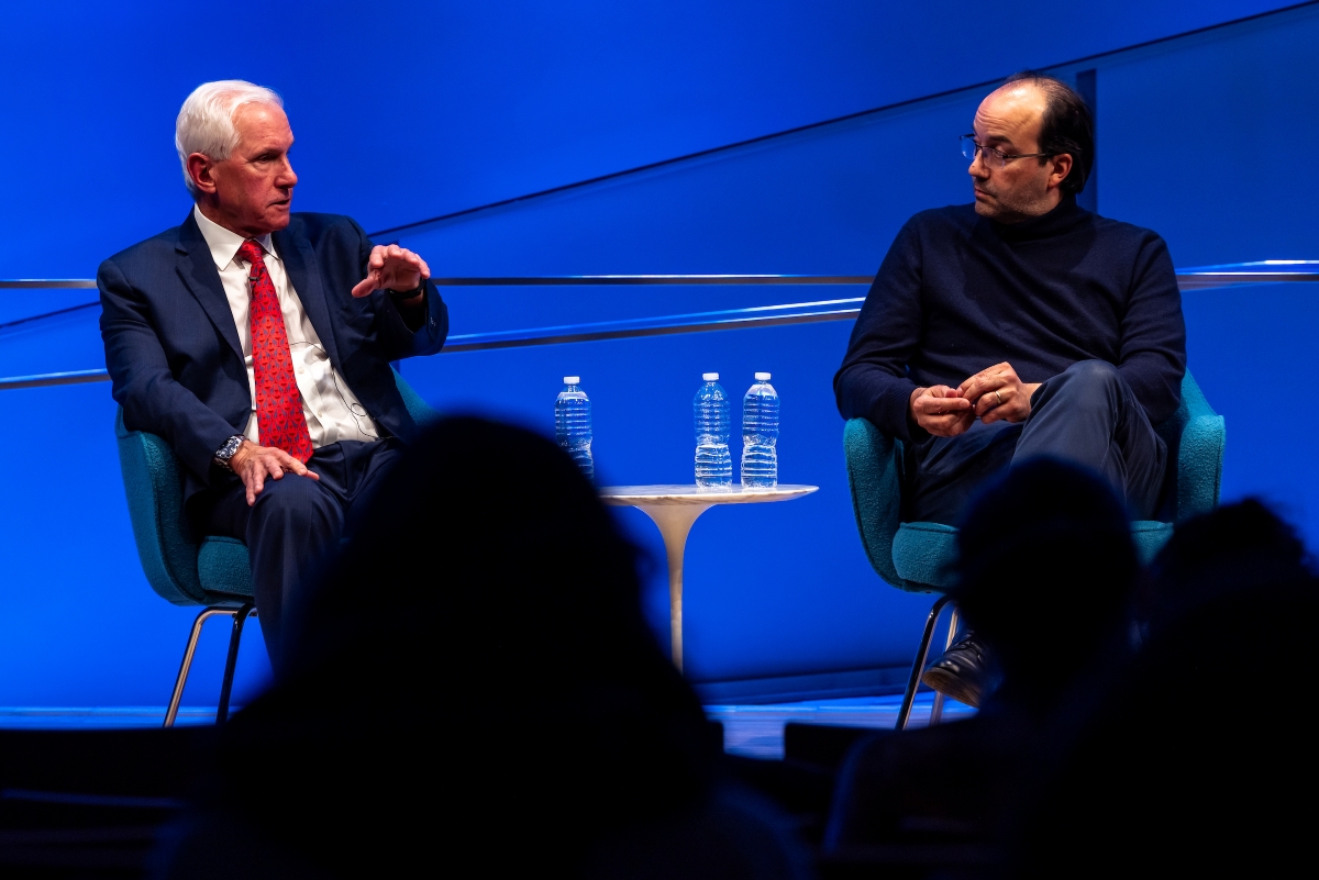 Two men speak on stage
