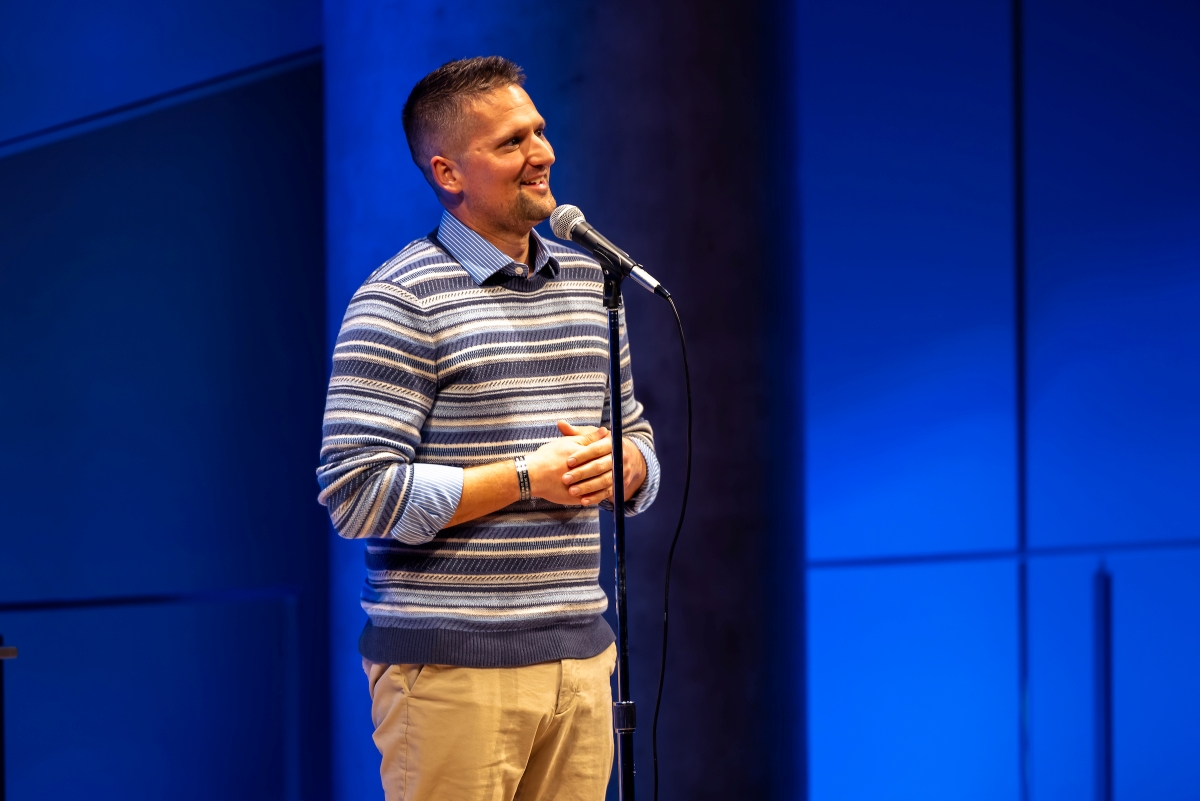 Man stands on stage speaking, clasping his hands 