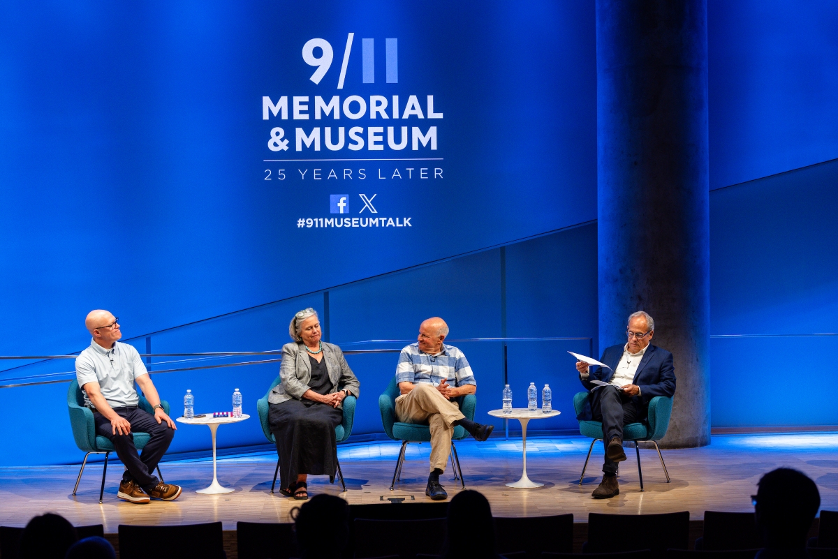 Wide stage with four people laughing under the 9/11 logo