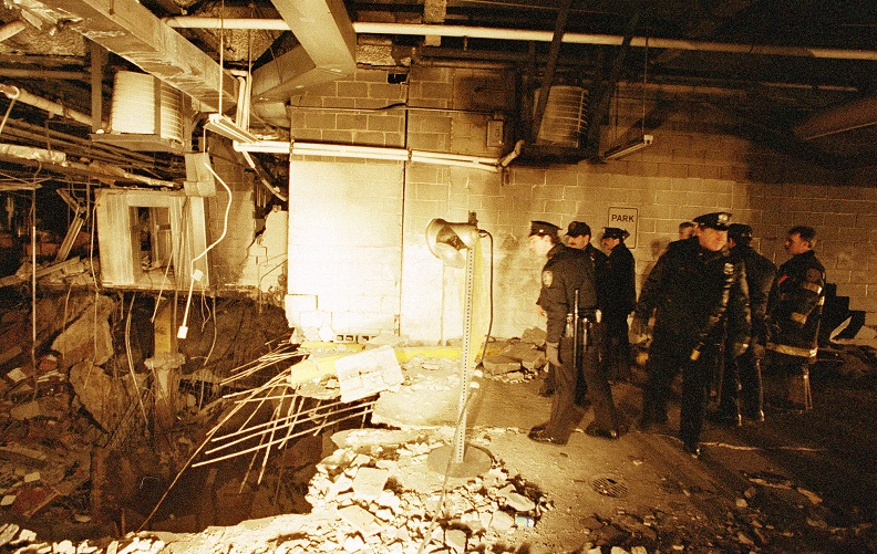  A historical photo of the 1993 World Trade Center bombing shows officers inspecting the crater left by the blast. The officers are standing to the right and looking down at  twisted rebar and crumbled concrete to the left 