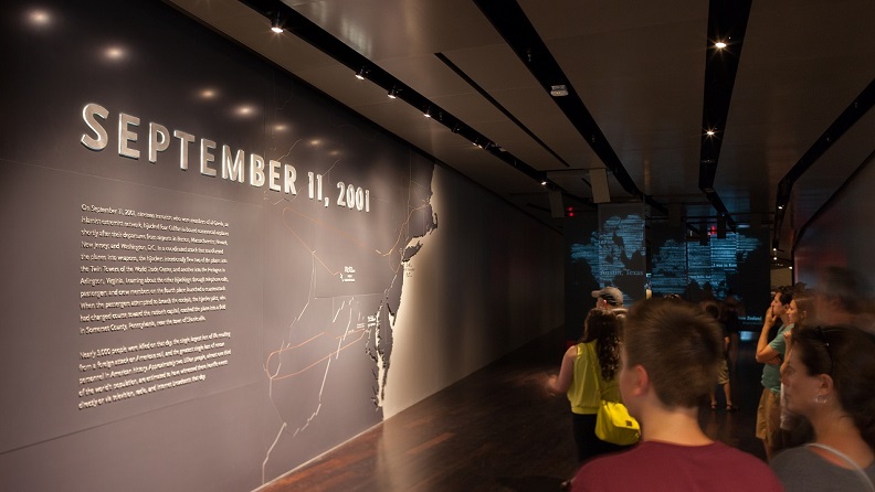 Visitors walk down a dimly lit hall. Beside them is a large map of the Eastern United States that shows the routes the hijacked planes took.