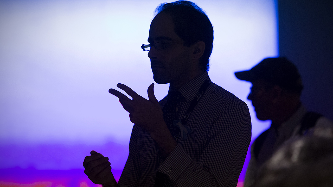 A man speaking in sign language is silhouetted against a bright screen at the Museum.