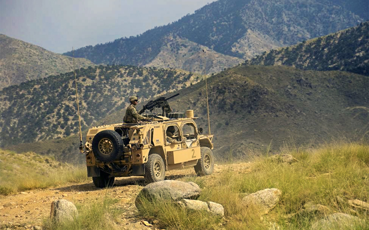 A soldier looks out on a mountainous terrain from an armored vehicle.