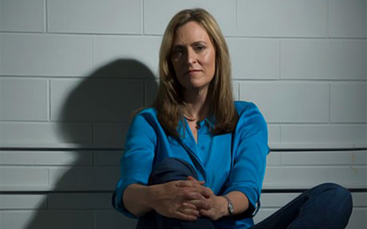 Former CIA analyst Nada Bakos poses for a portrait in front of a white brick wall.
