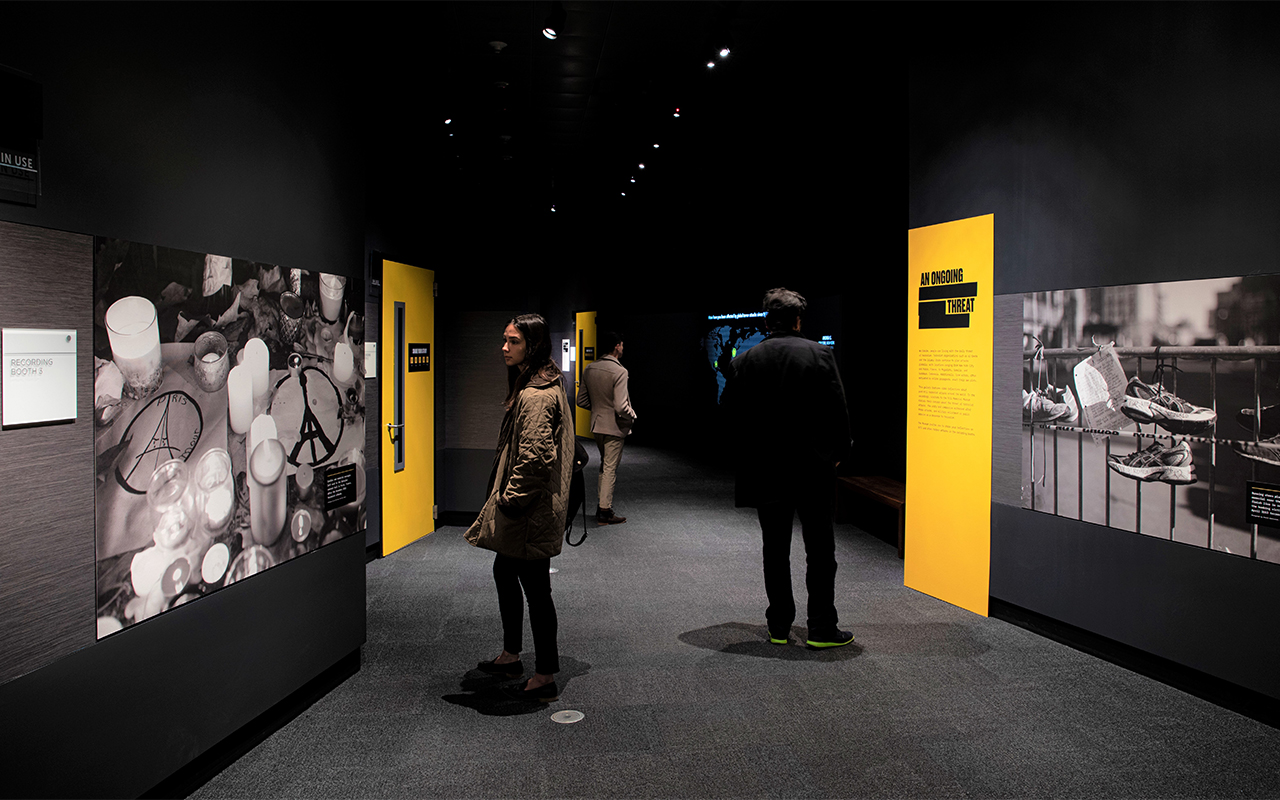 Three people stand staggered in a dark room, looking at large-format black-and-white photos.