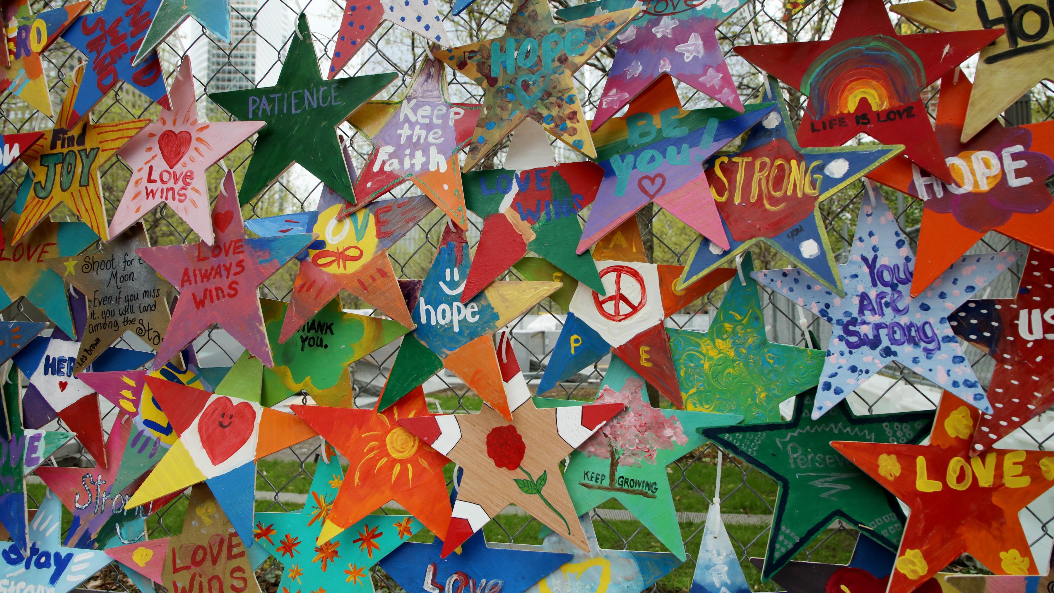 An array of hand-crafted Stars of Hope decorate a fence near the 9/11 Memorial plaza. The stars bear messages such "Peace," "Keep the Faith," and "Love Wins."