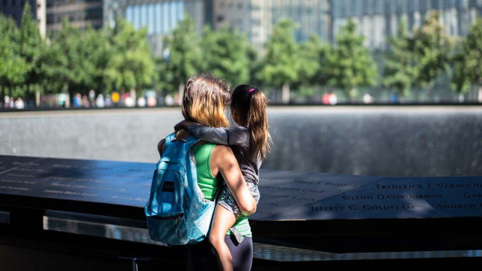 Image of the back of a woman holding a young girl while looking at the Memorial parapet on a sunny day 