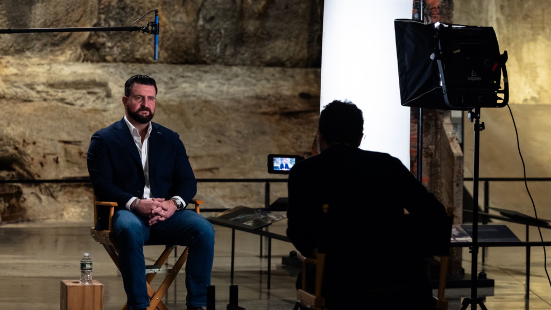 An interview subject sits in a director's chair in front of a camera. 