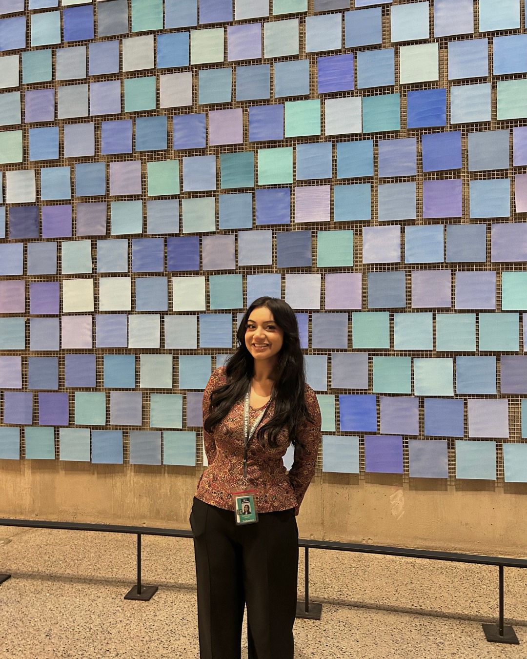 A woman stands in front of a wall of tiles in different shades of blue. 