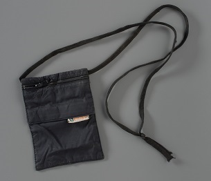 A black case with a neck strap, used for travel documents, is displayed on a gray background. It was worn by Flight 93 passenger Toshiya Kuge.