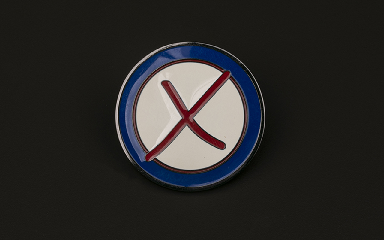 A challenge coin with a raised red X in the center of an ivory circle and a navy blue border is suspended against a black background.