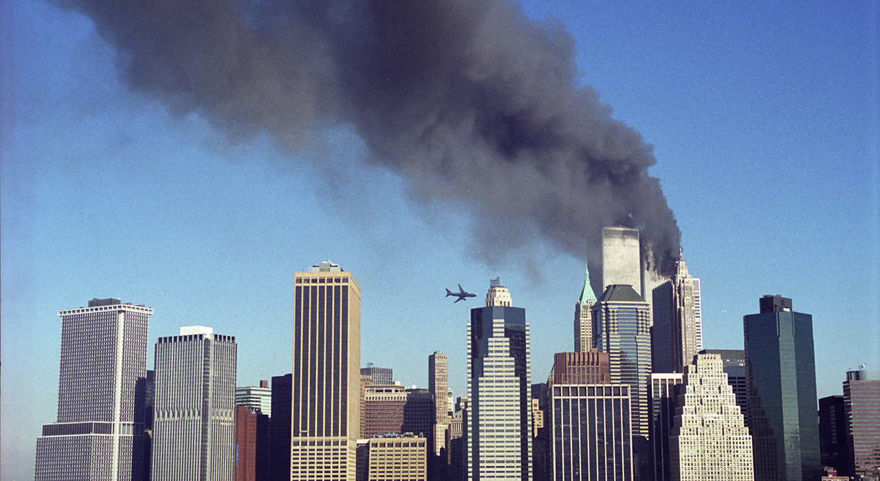 An airplane is flying towards one of the Twin Towers while black smoke billows out the other tower.