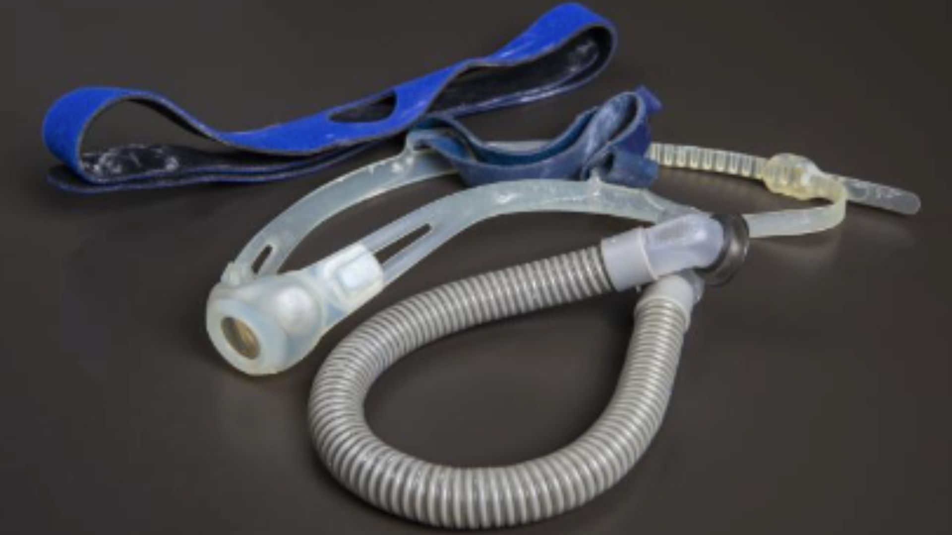 ResMed "nasal pillow" breathing mask with a blue fabric headband and clear plastic nasal "pillows." A short gray accordion breathing tube is attached.