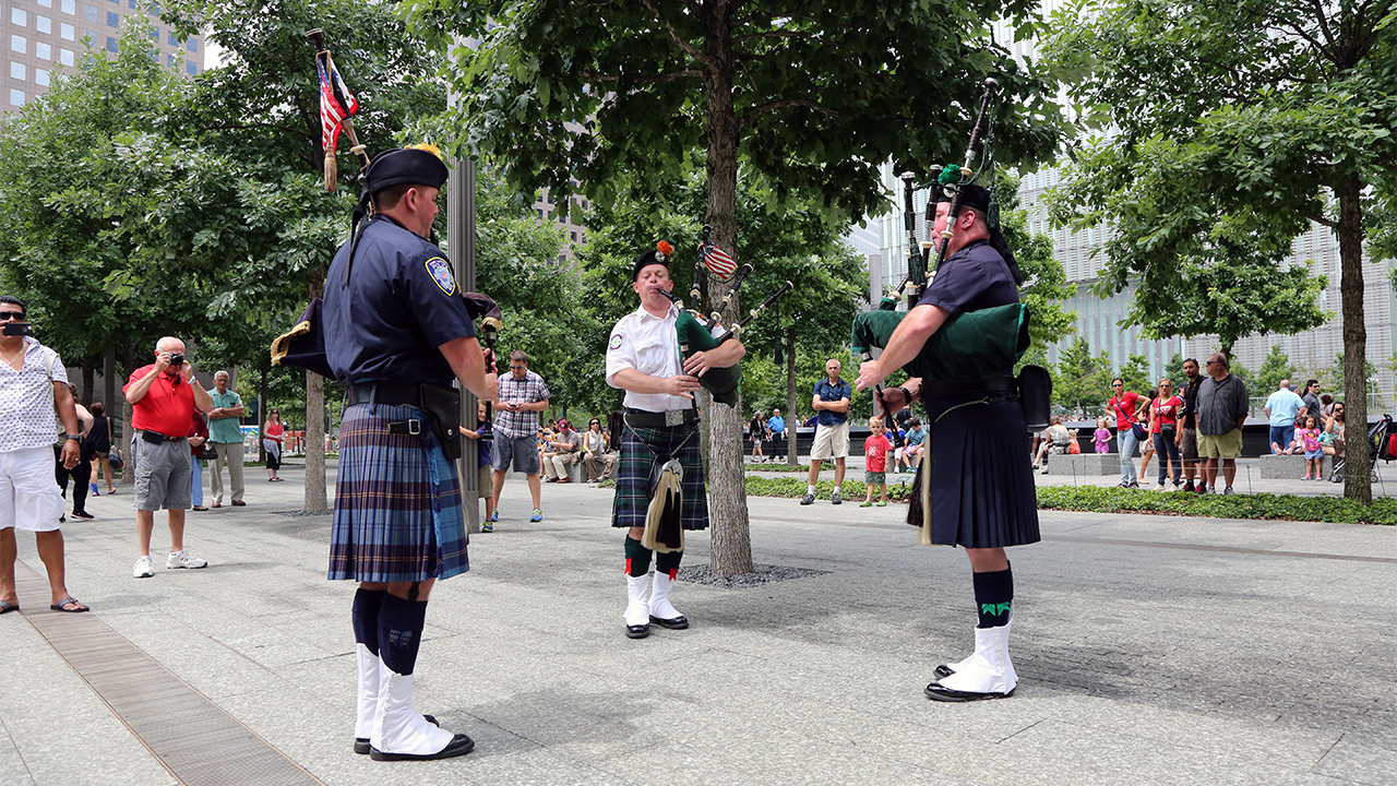 three bagpipers play on the Memorial while people watch and take pictures