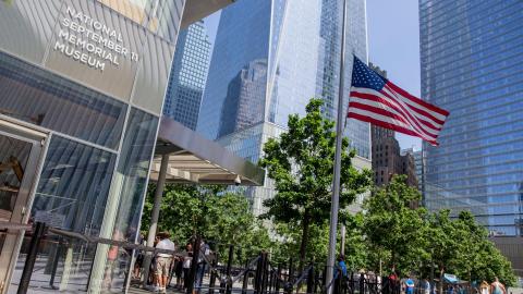 Entrance to the 9/11 Museum, with an American flag gently blowing in breeze and leafy green trees in foreground