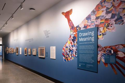 Children's artwork on display on a blue wall, with an exhibition sign in the foreground