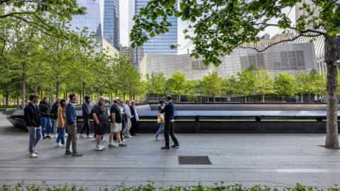 A group listens to a tour guide in front of a Memorial  pool on the plaza